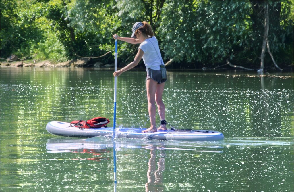 woman in white shirt and blue shorts standing on blue standup paddle board during daytime